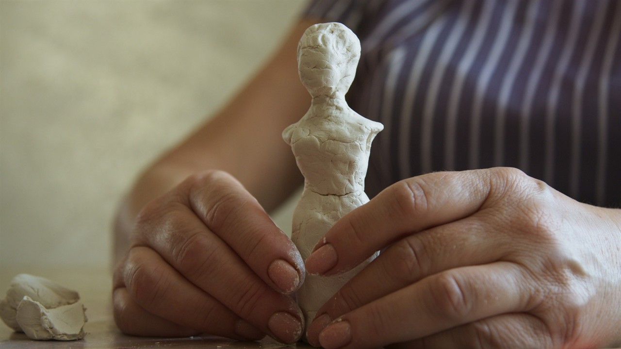 Hands making a clay sculpture of a person